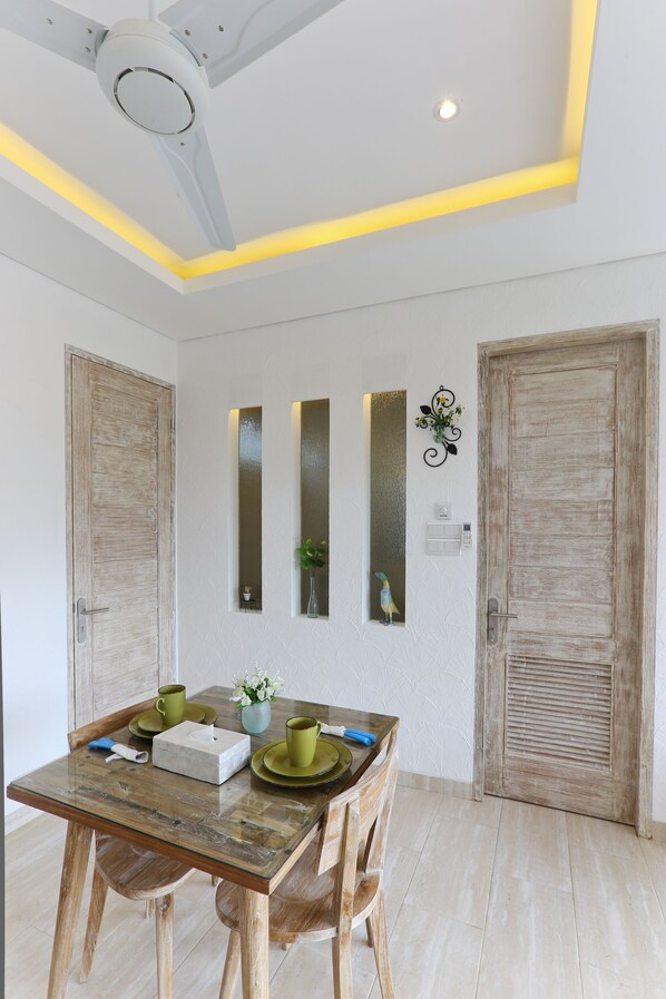 A dining area with a wooden table, chairs, and a ceiling fan. There are three vertical mirrors on the wall and a door with a rustic finish.