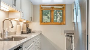 Uma cozinha compacta com forno embutido, geladeira de aço inoxidável e janela com moldura de madeira.