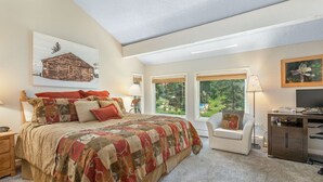 Quarto com uma cama grande, uma escrivaninha, uma cadeira e uma televisão.