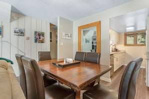 Een eetgedeelte met een houten tafel, lederen stoelen en een keuken op de achtergrond.