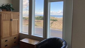 A room with a view of the ocean through large windows, a wooden cabinet, and a black leather chair. - All About the View North 3 bedroom oceanfront (Bandon)