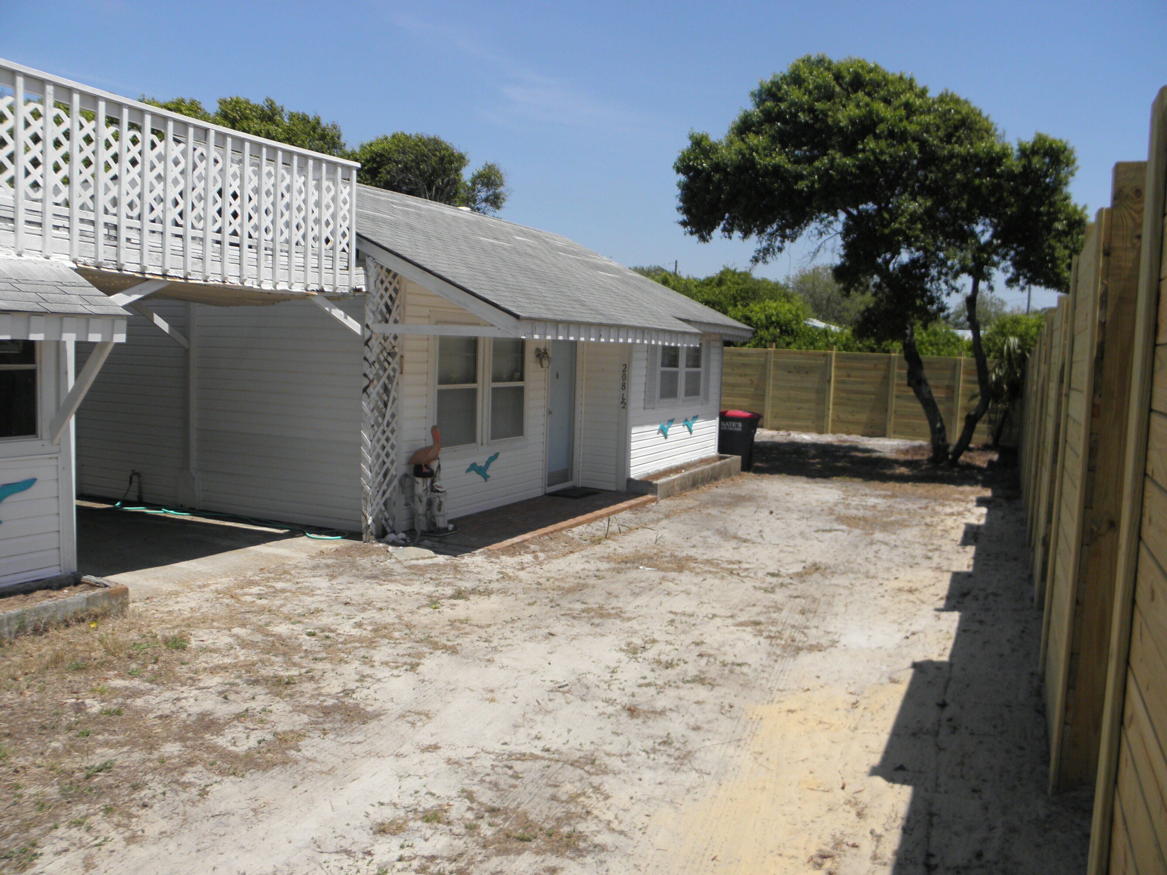 A small, single-story house with a white exterior, a porch, and a fenced backyard.