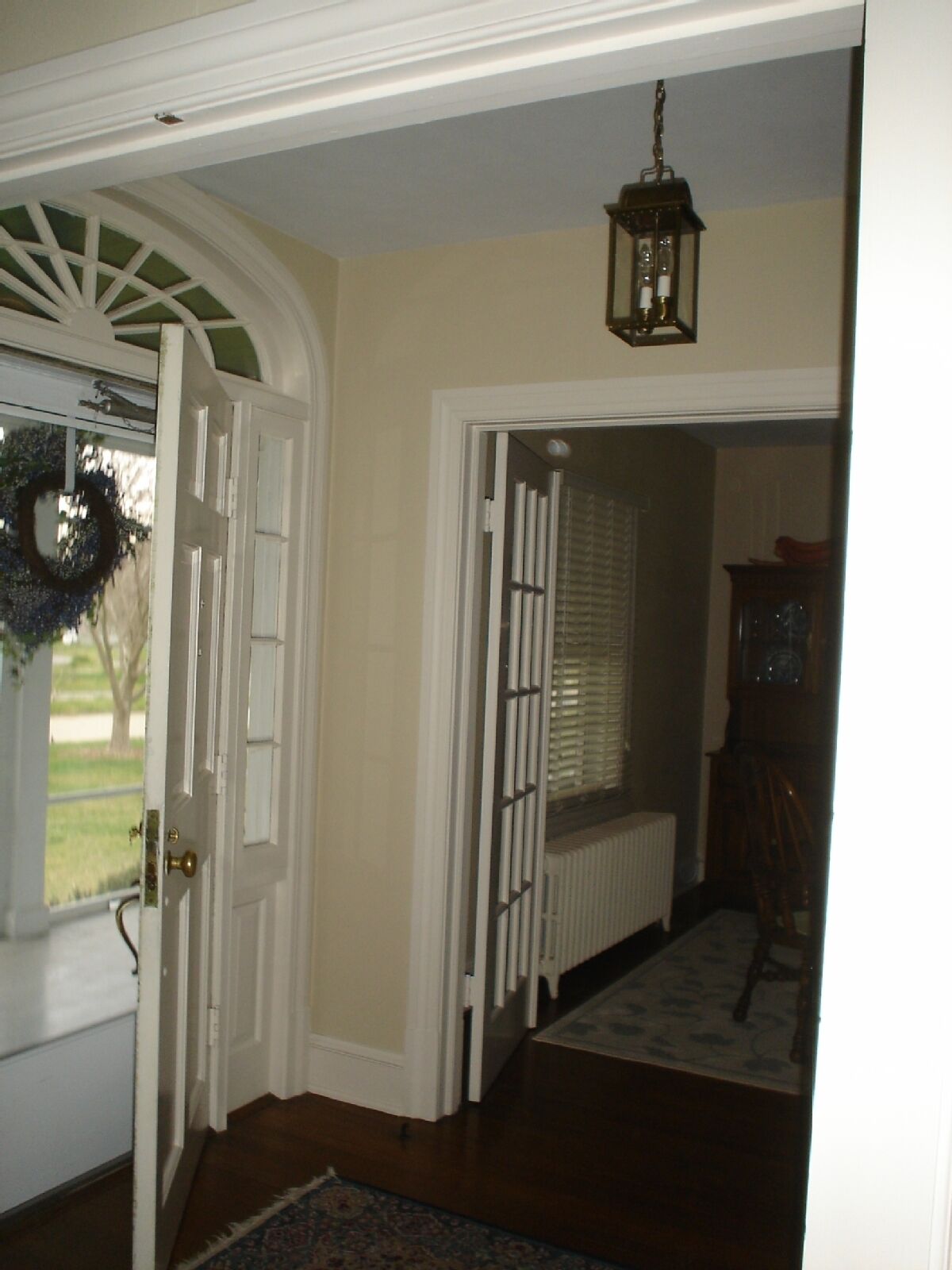 A hallway with a white door, a radiator, a wooden chair, and a hanging lantern.