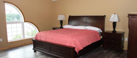 A bedroom with a large bed, two nightstands, a dresser, and a window with a view.