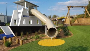 A playground with a slide, a climbing structure, and a wooden swing set. - Palm Court Motel (Otorohanga)