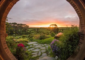 Un arco de piedra rústico enmarca un jardín exuberante con vistas a la puesta de sol.