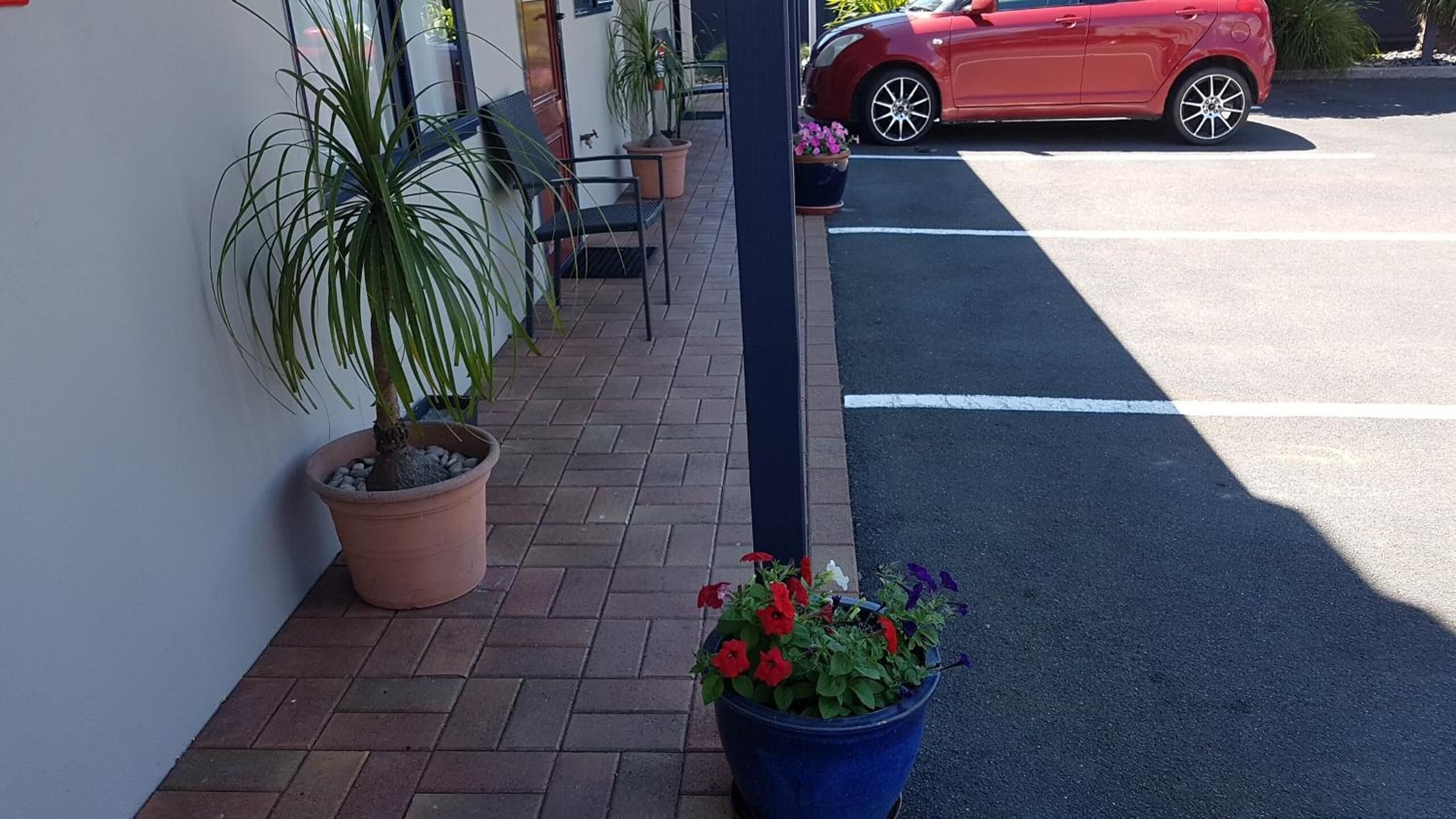 A parking area with a red car, potted plants, and a blue flower pot.