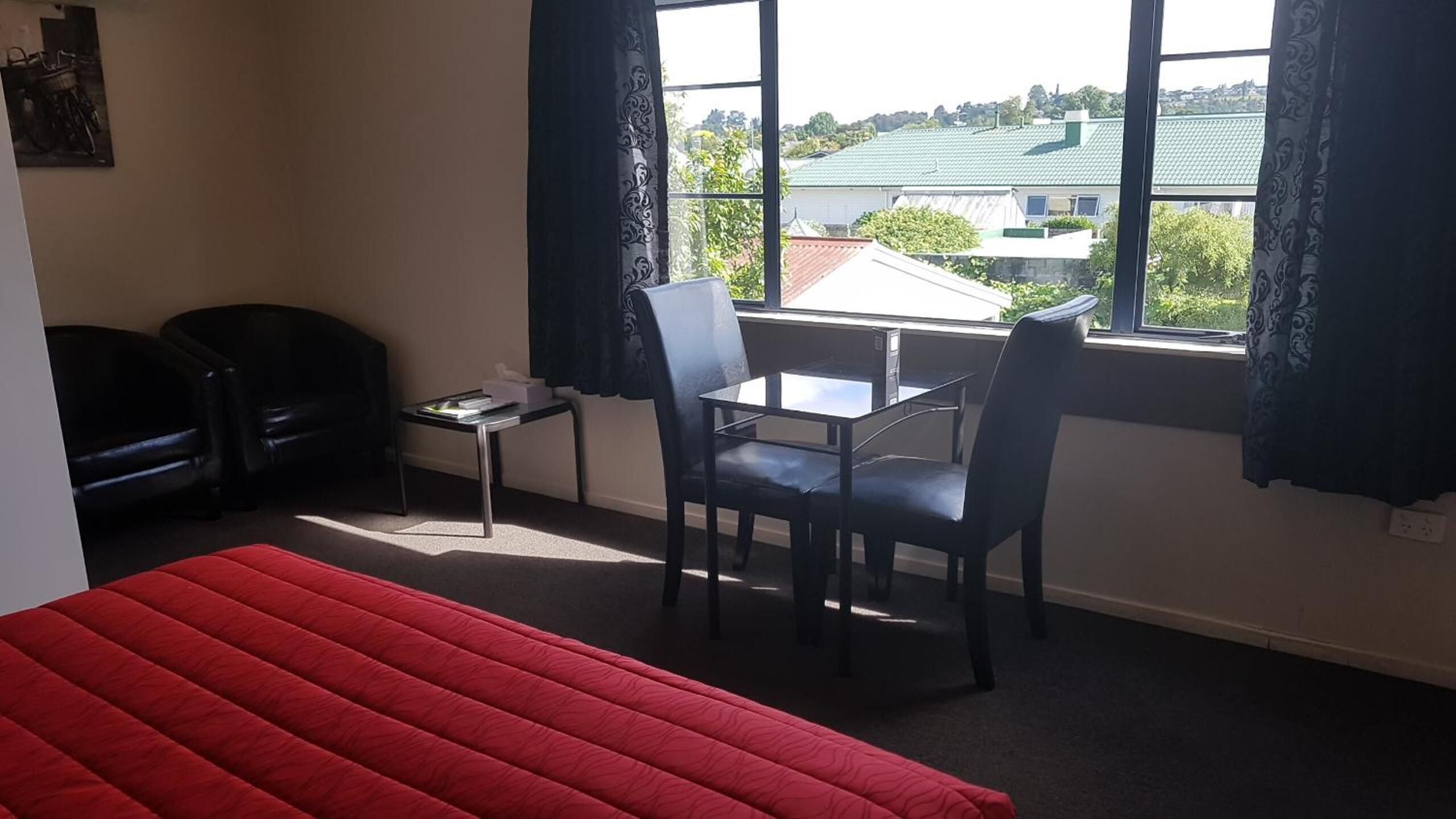 A room with a bed, a desk, two chairs, and a window with curtains.