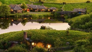 A rural village with thatched-roof cottages, a pond, and a stone bridge. - Palm Court Motel (Otorohanga)