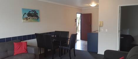 Una habitación con una mesa de comedor y sillas, un sofá, un cuadro en la pared y una puerta que da a otra estancia.