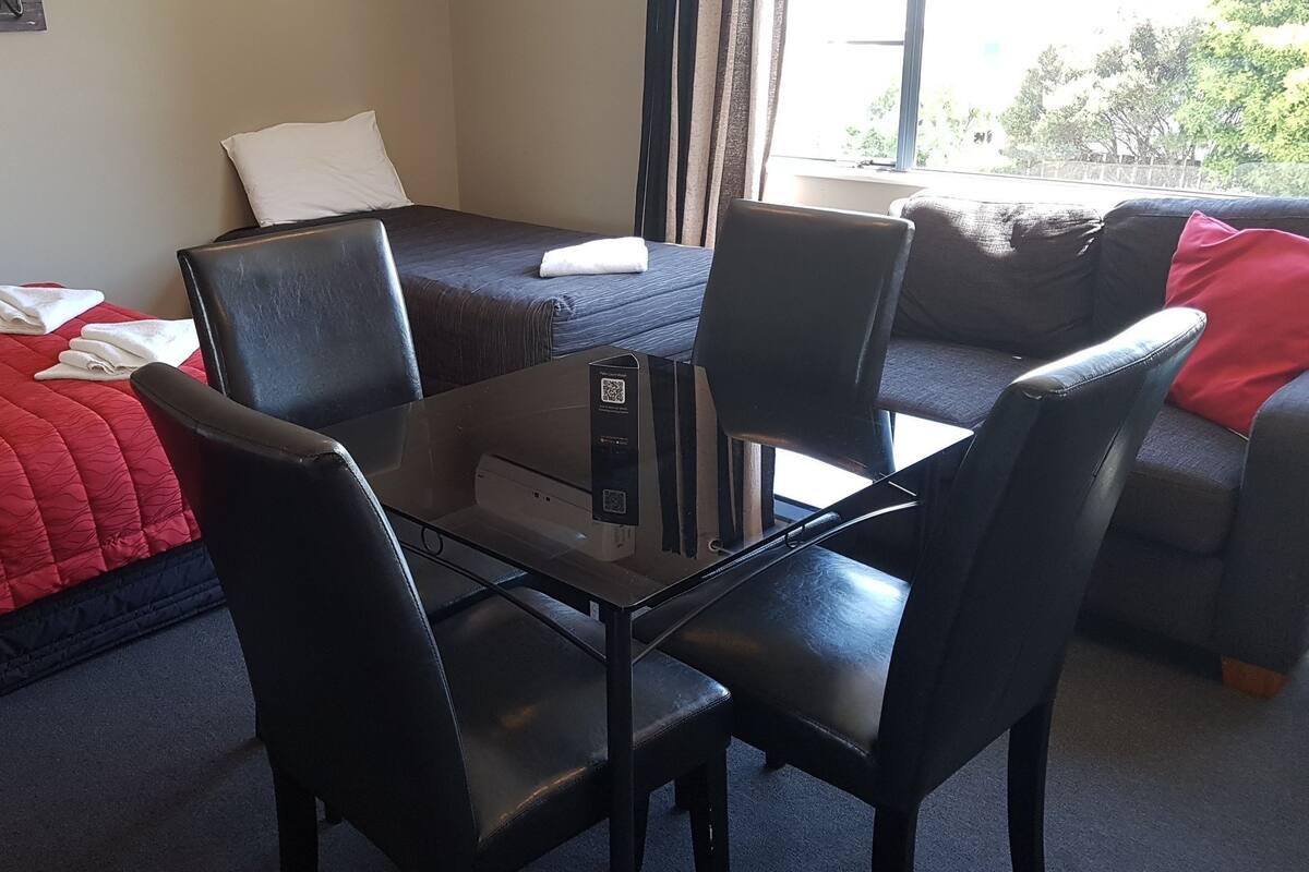 A hotel room with a bed, a sofa, a dining table with chairs, and a window with curtains.