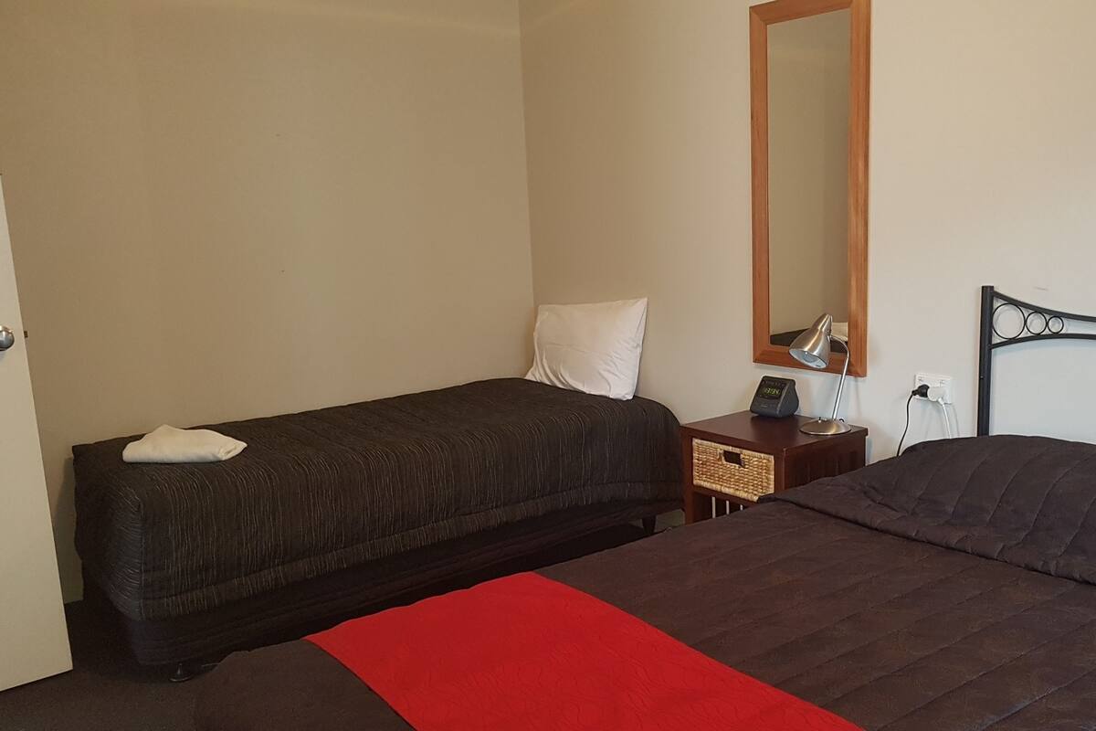 A bedroom with two beds, a bedside table with a lamp, a mirror, and a red throw blanket.