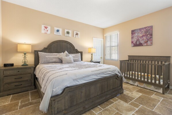 A bedroom with a wooden bed, two bedside tables with lamps, a crib, and artwork on the walls.