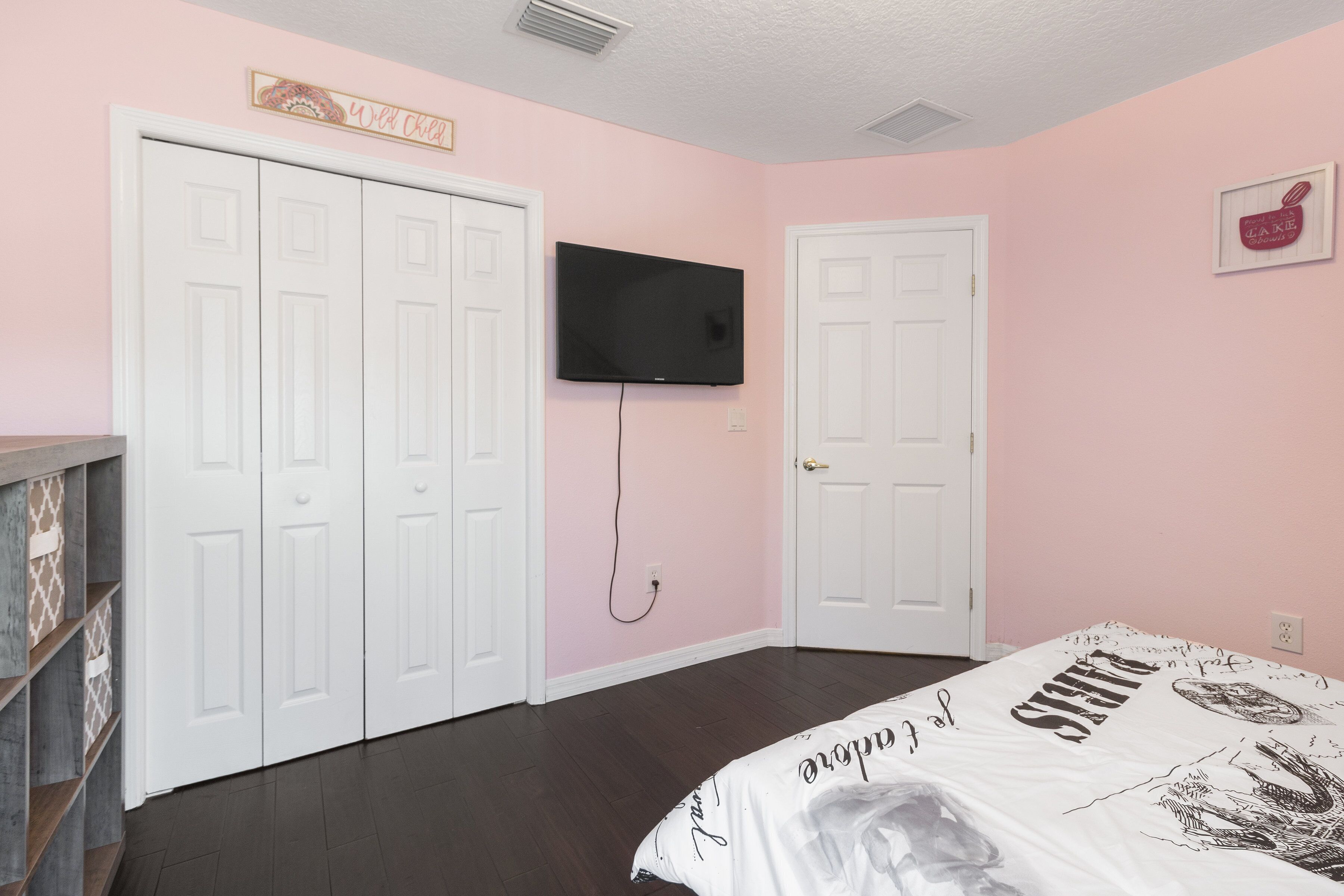 Une chambre à coucher avec un lit, un téléviseur fixé au mur et une porte.