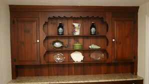Un mueble de cocina de madera con estantes que contienen botellas, una jarra y diversos utensilios de cocina.