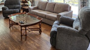 Una sala de estar con sofá, sillones, una mesa de centro de vidrio y una lámpara.