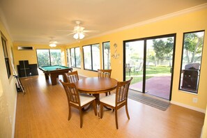 Amplia habitación con mesa de billar, comedor y sillas, ventanas grandes y ventilador de techo.