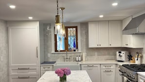 A modern kitchen with white cabinetry, a marble island, and a stainless steel stove. - Charming Nantucket home. (Nantucket)