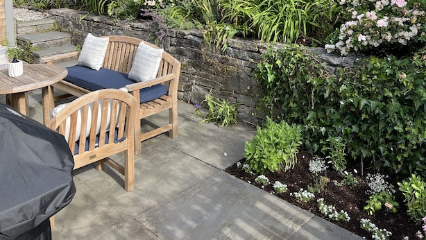 A patio with wooden furniture, a stone wall, and a variety of flowering plants. - Charming Nantucket home. (Nantucket)