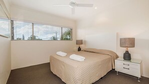 A bedroom with a bed, two bedside tables, a ceiling fan, and a window with blinds. - Whale season is upon us, watch from your balcony (SUNSHINE BEACH)