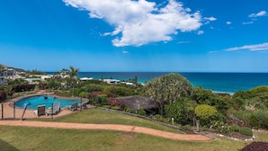 A pool area with a view of the ocean, surrounded by greenery and a clear sky. - Whale season is upon us, watch from your balcony (SUNSHINE BEACH)