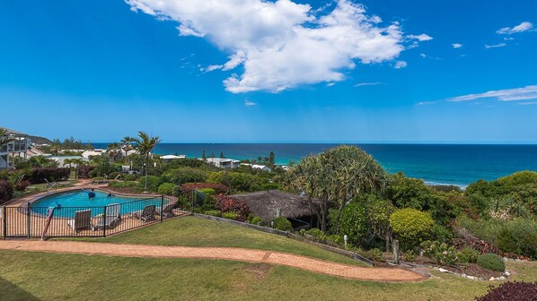 A pool area with a view of the ocean, surrounded by greenery and a clear sky. - Whale season is upon us, watch from your balcony (SUNSHINE BEACH)