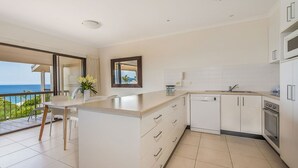 A modern kitchen with a large island, white cabinetry, and a view of the ocean. - Whale season is upon us, watch from your balcony (SUNSHINE BEACH)