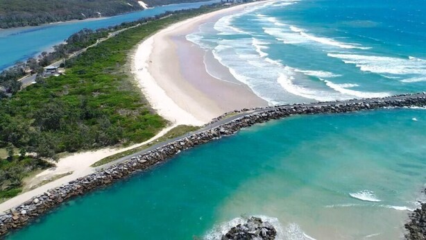 An aerial view of a coastal area with a sandy beach, a rocky breakwater, and clear turquoise waters. - Two Bedroom House Wooli (Wooli)