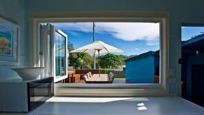 A kitchen with a large window overlooking a patio area with outdoor furniture and an umbrella. - Two Bedroom House Wooli (Wooli)