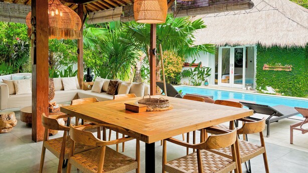 A wooden dining table with chairs, a sofa, and a pool in the background. - Traditionally Designed Seminyak Villa with Garden (Badung)