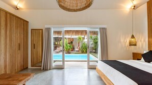 A bedroom with a large bed, a wooden wardrobe, a dining table, and a view of an outdoor swimming pool. - Traditionally Designed Seminyak Villa with Garden (Badung)