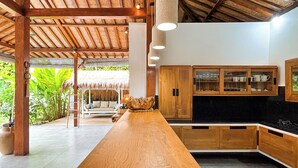 A kitchen with wooden cabinets, a central island, and a thatched roof structure. - Traditionally Designed Seminyak Villa with Garden (Badung)