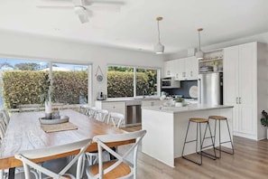 A modern kitchen with white cabinetry, a wooden dining table, and two bar stools.
