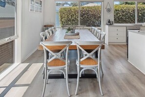 A dining area with a long table, white chairs, and a view of a hedge outside. - Millos by the Sea (Sorrento)