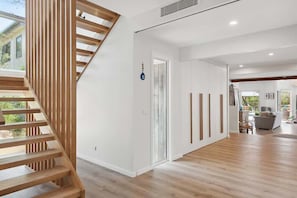 A modern interior with a wooden staircase, a door with a keyhole, and a view of the outdoors.
