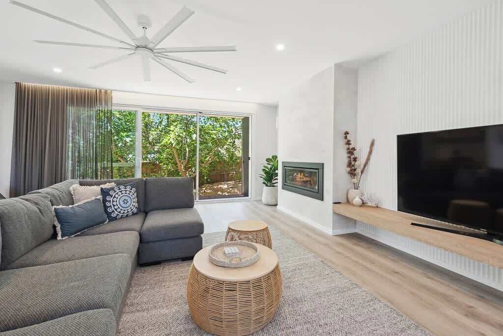 Un salon moderne avec un canapé d’angle, un téléviseur à écran plat et un ventilateur de plafond.