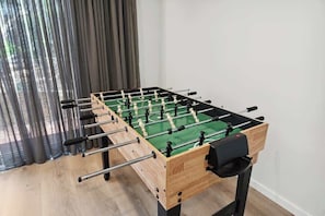 A foosball table in a room with a wooden floor and a window with curtains.