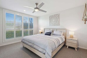 A bedroom with a bed, a ceiling fan, a nightstand, and a window with blinds.