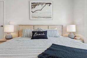 A bed with a headboard, two bedside lamps, a pillow with 'Beach' text, and a framed picture of a beach scene. - Millos by the Sea (Sorrento)
