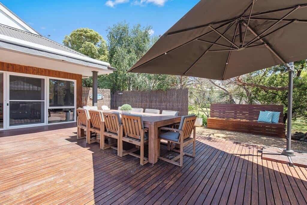 An outdoor deck with a wooden table and chairs, a large umbrella, and a wooden fence in the background.
