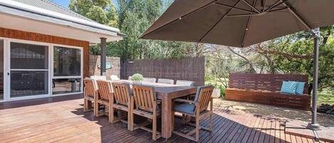 An outdoor deck with a wooden table and chairs, a large umbrella, and a wooden fence in the background.