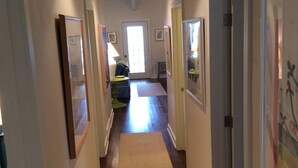 Un couloir aux murs ornés de tableaux encadrés, doté d’un sol recouvert de moquette et de portes donnant sur d’autres pièces.