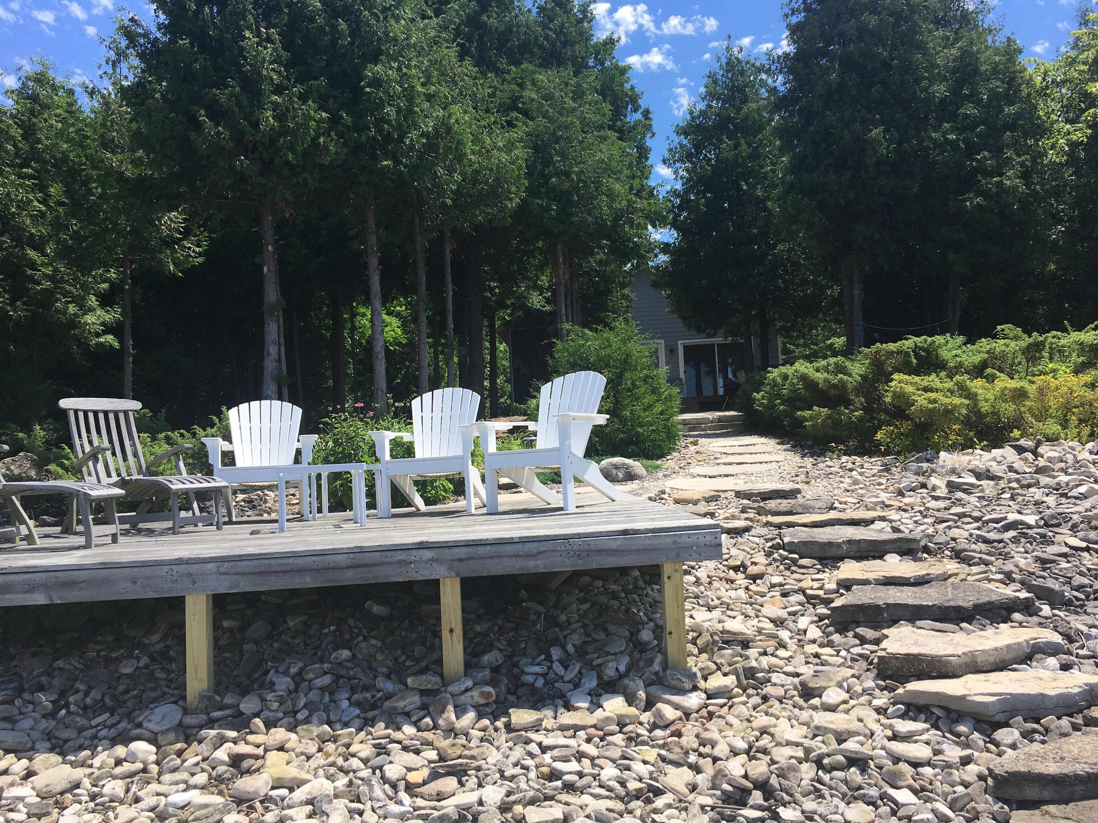 A wooden deck with white Adirondack chairs, surrounded by a rocky landscape and dense trees.