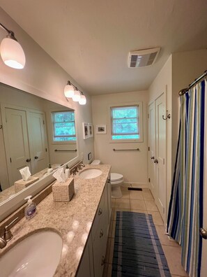 Une salle de bain avec deux lavabos, un grand miroir, une fenêtre et un rideau de douche.