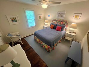 Une chambre à coucher comprenant un lit, deux tables de chevet, une chaise, un ventilateur de plafond et une fenêtre.