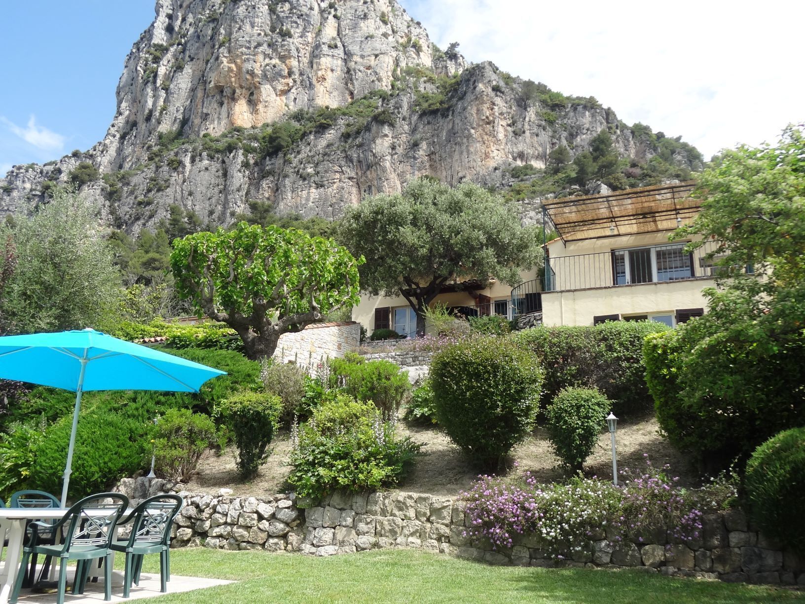 A patio area with a table and chairs, a blue umbrella, and a stone wall.