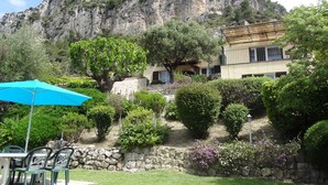 Un patio con mesa y sillas, una sombrilla azul y un muro de piedra.