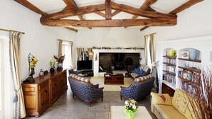 Un salón amplio con vigas de madera, una chimenea, un televisor y una estantería.