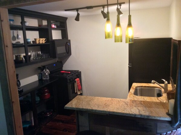 A compact kitchen with a granite countertop, a stainless steel sink, and hanging pendant lights.