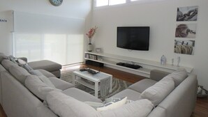 A modern living room with a large sofa, a flat-screen TV, and a bookshelf. - Genesta Street, sleeps 14 people, in the heart of Cowes (Cowes)